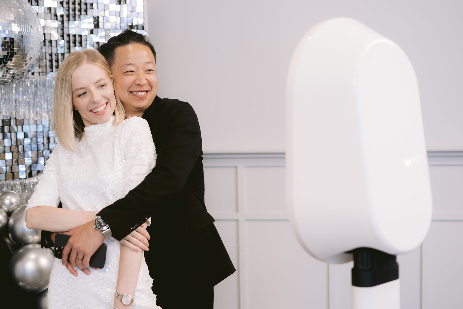 A couple embracing and laughing beside the Mosaic photo booth at a party